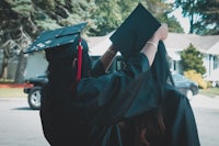 two women in graduation gowns putting on their hats