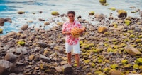 a man holding a watermelon on a rocky beach