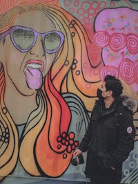 a man standing in front of a mural of a woman wearing sunglasses