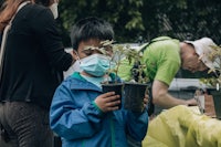 a boy wearing a face mask holds a potted plant