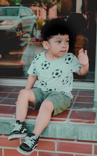 a young boy sitting on a ledge in front of a brick building