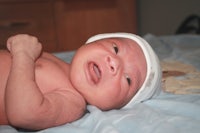 a baby in a white hat laying on a bed