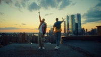 two men standing on top of a roof overlooking a city