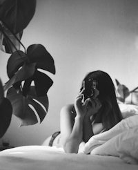 a black and white photo of a woman taking a picture in bed