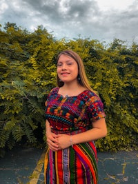 a woman in a colorful dress standing in front of bushes